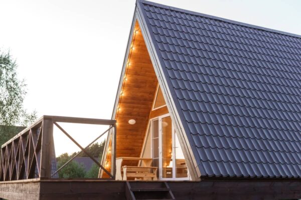 Domek z drewnianym tarasem i dachem pokrytym blachodachówką.