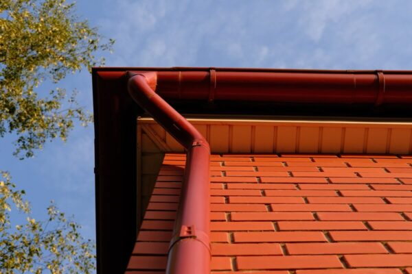 Czerwone rynny stalowe na tle nieba i ceglanej ściany.