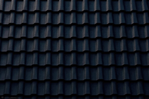 Widok ciemnej powierzchni, na której ułożona jest dachówka cementowa.