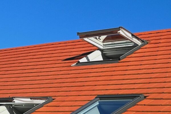 Czerwona dachówka na dachu wykonana jest z płyt warstwowych z oknami dachowymi.